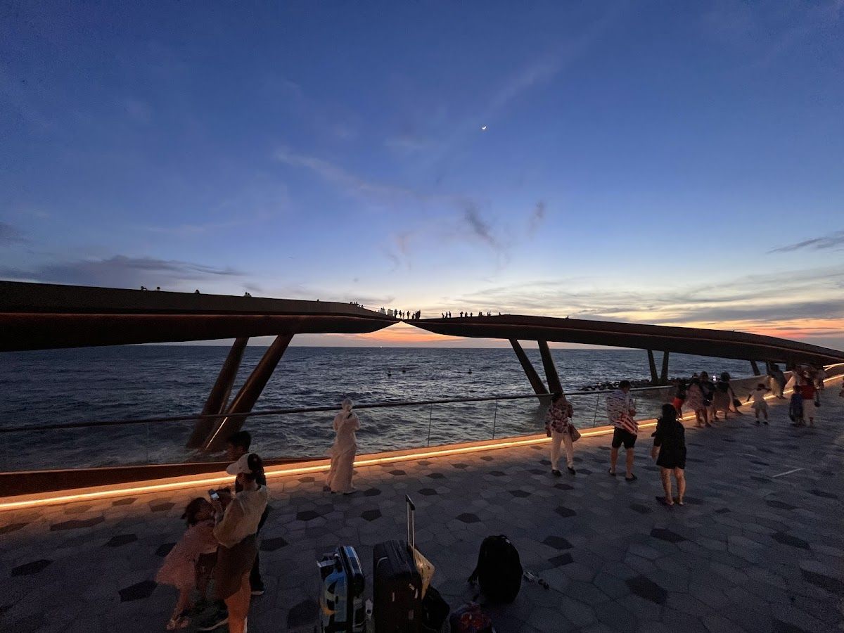 Kiss Bridge at Sunset Town in An Thoi at dusk, visitors walking along the curved seaside walkway above the ocean